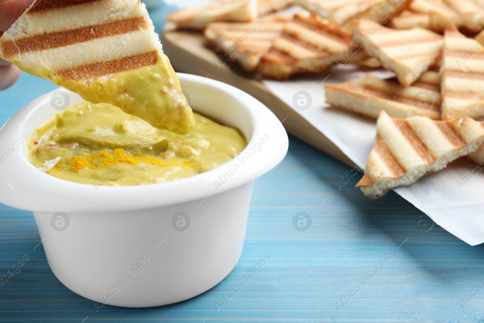 Photo of Dipping pita chip into hummus on light blue wooden table, closeup