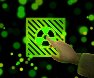 Image of Man touching glowing radiation warning symbol on black background with blurred green and yellow lights, closeup