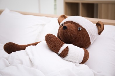 Photo of Toy bear with bandages lying in bed indoors