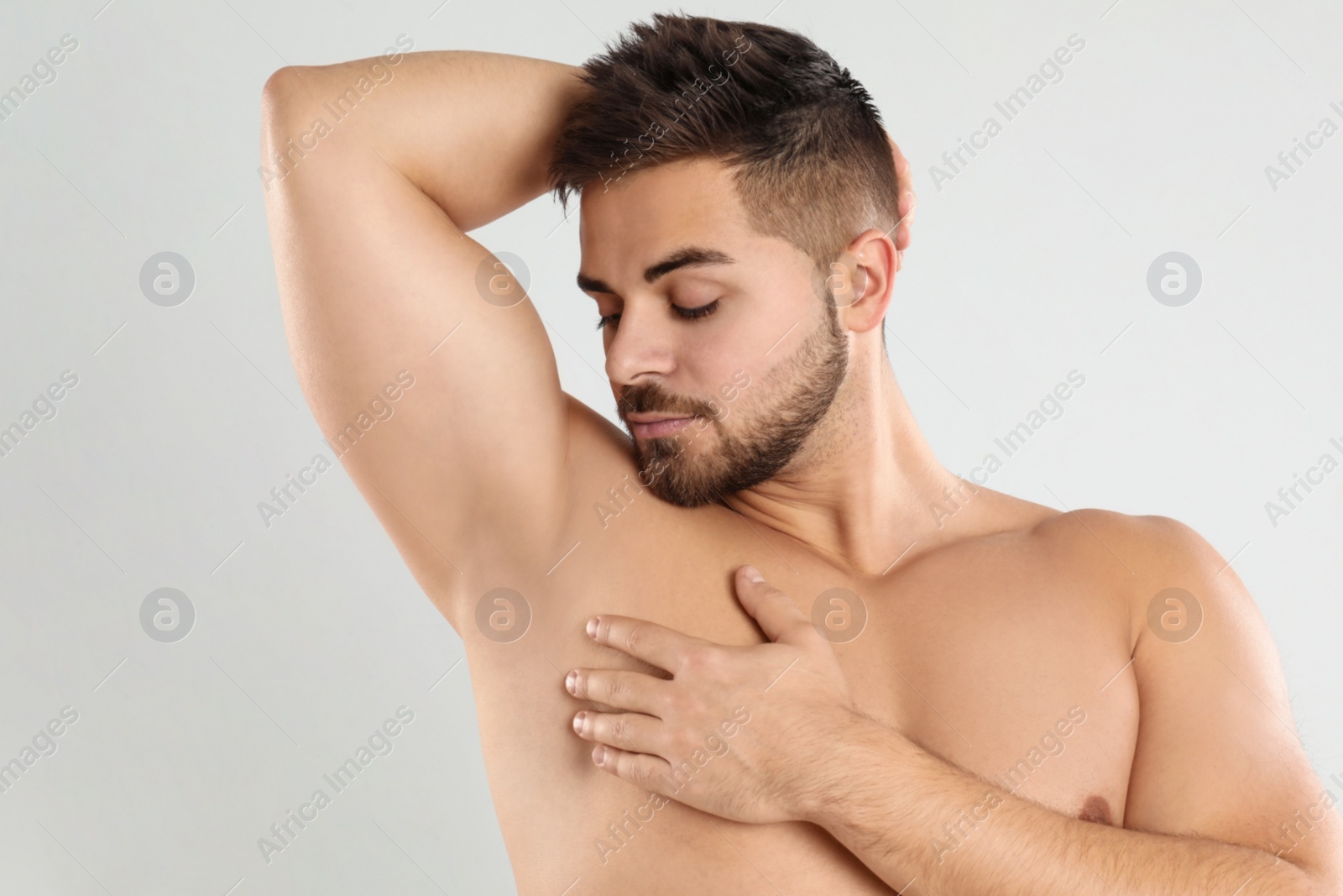 Photo of Young man showing hairless armpit after epilation procedure on light grey background