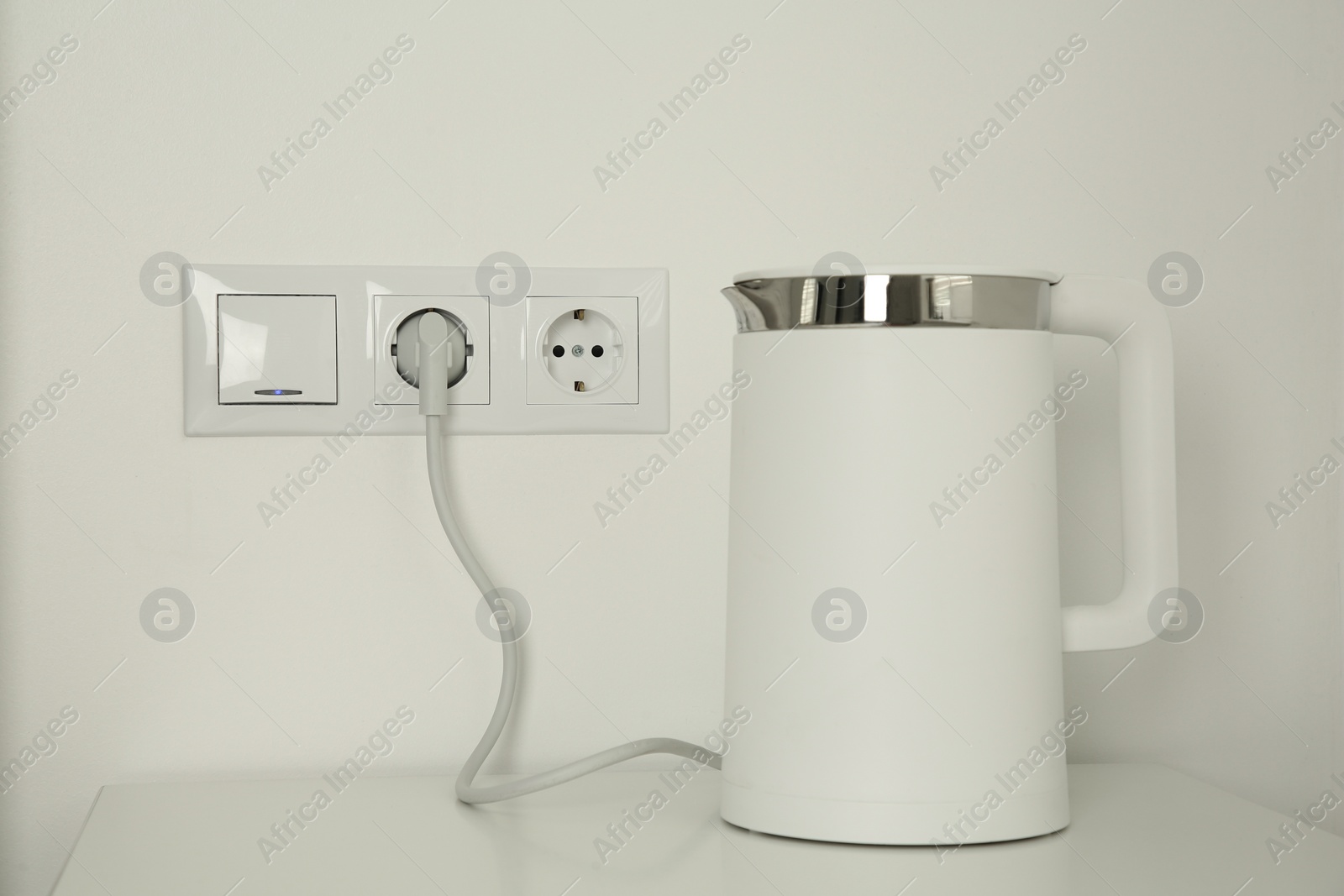 Photo of Electric kettle plugged into power socket on white wall