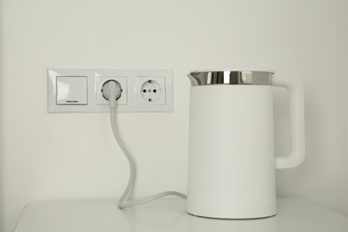 Photo of Electric kettle plugged into power socket on white wall