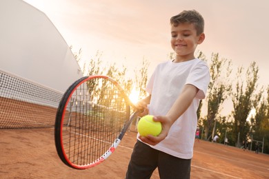 Photo of Cute little boy playing tennis on court outdoors