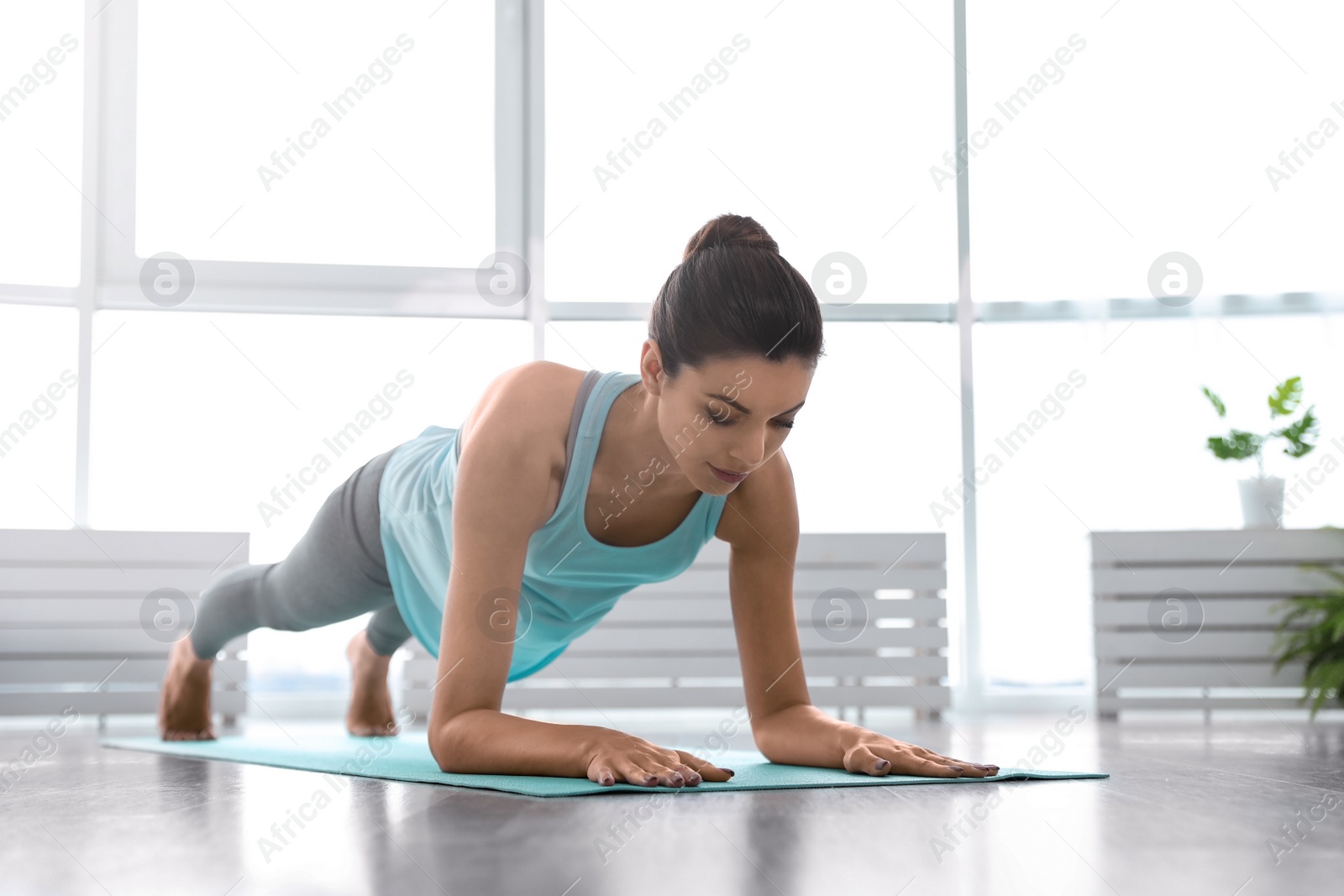 Photo of Young woman practicing forearm plank asana in yoga studio. Phalakasana variation pose