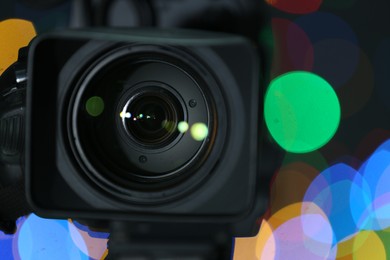 Modern video camera against blurred colorful lights, closeup