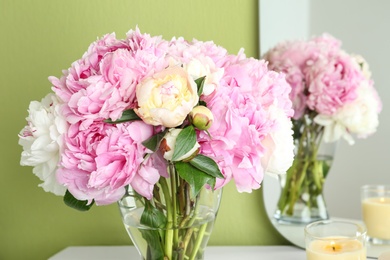 Photo of Beautiful peonies and candle on white dressing table near green wall