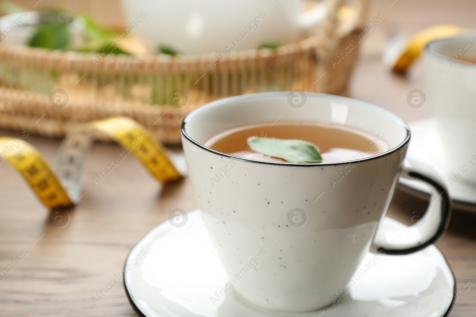 Photo of Cup of herbal diet tea and measuring tape on wooden table, closeup