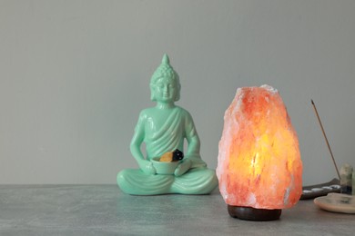 Photo of Himalayan salt lamp, buddha figure, incense and crystals on stone table near grey wall, space for text