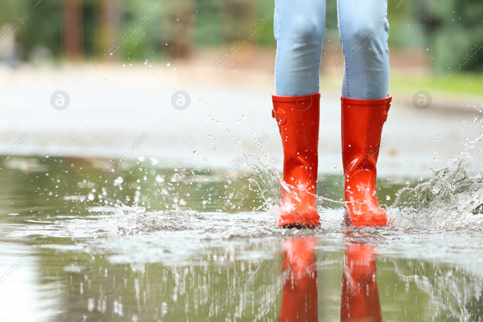 Photo of Woman with red rubber boots jumping in puddle, closeup. Rainy weather