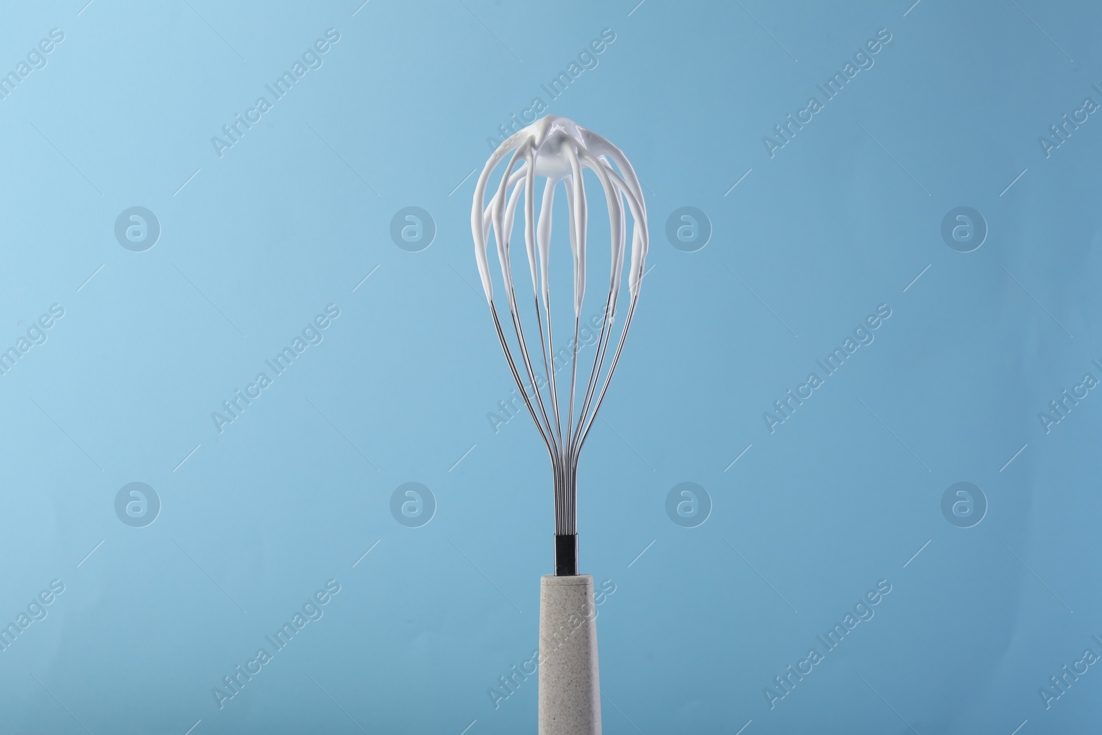 Photo of Whisk with whipped cream on light blue background
