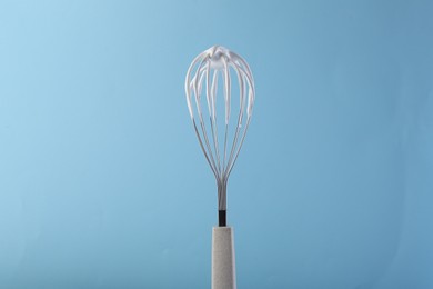 Whisk with whipped cream on light blue background