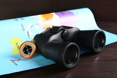 Photo of Modern binoculars, compass and map on wooden table, closeup