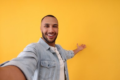 Photo of Smiling young man taking selfie on yellow background, space for text