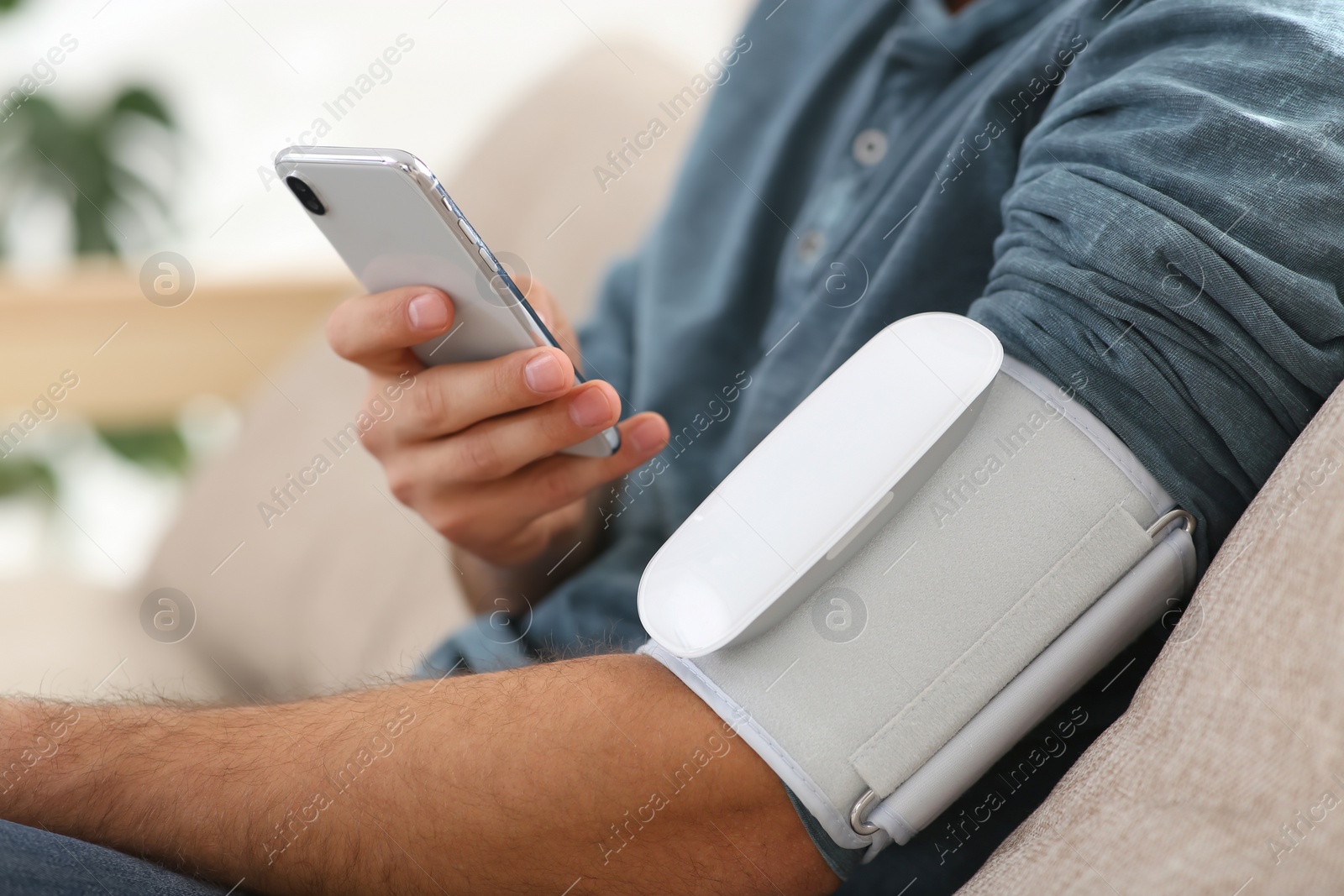 Photo of Man checking blood pressure with modern monitor and smartphone indoors, closeup