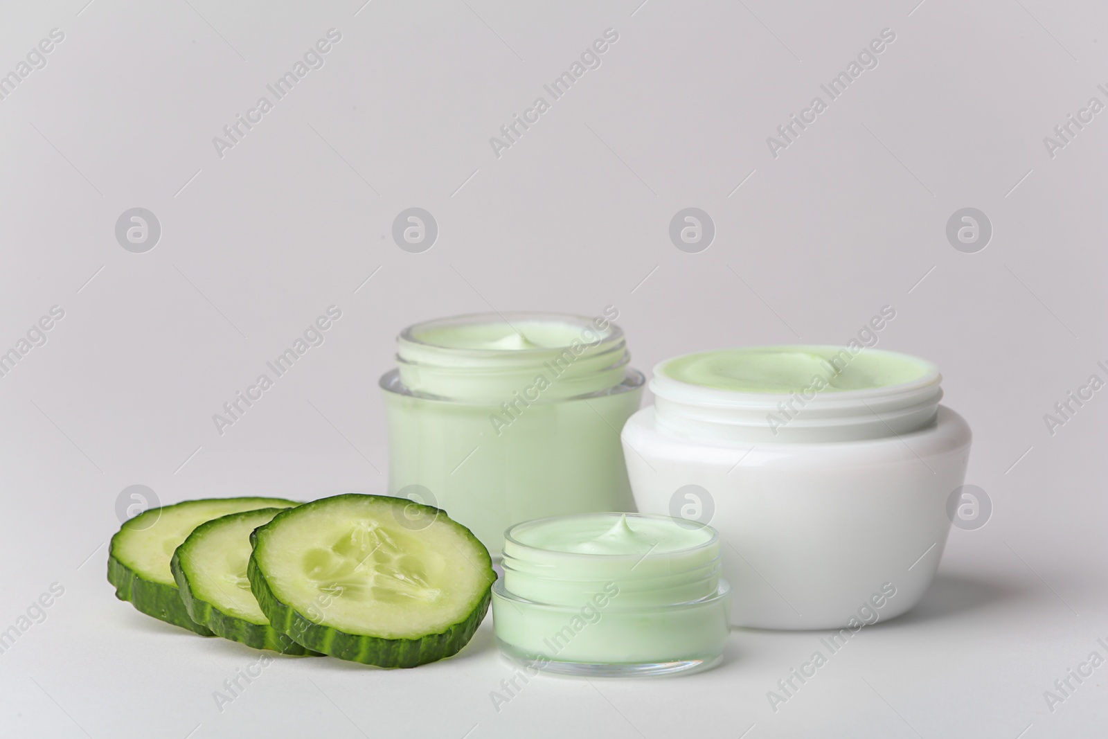 Photo of Jars of body cream and cucumber slices on white background