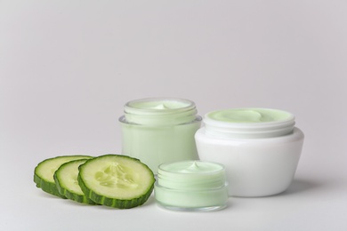 Photo of Jars of body cream and cucumber slices on white background