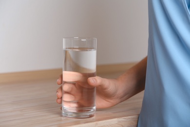 Photo of Woman holding glass with fresh water on wooden table, closeup