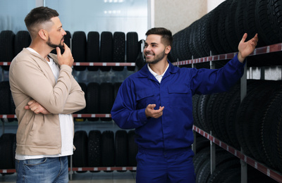 Photo of Mechanic helping client to choose car tire in auto store