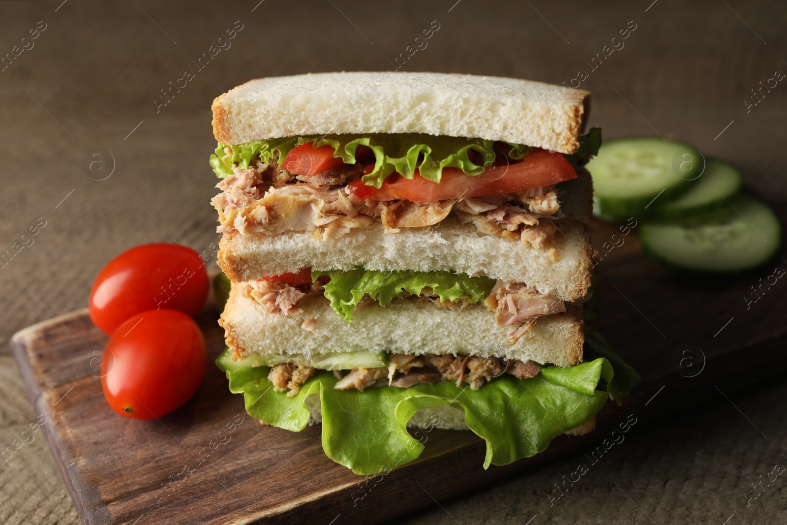 Photo of Delicious sandwich with tuna, tomatoes and lettuce on wooden table, closeup