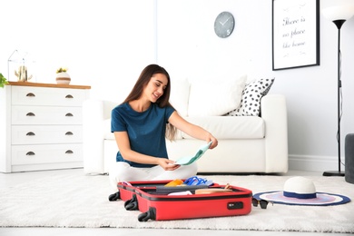 Photo of Young woman packing suitcase for summer journey at home