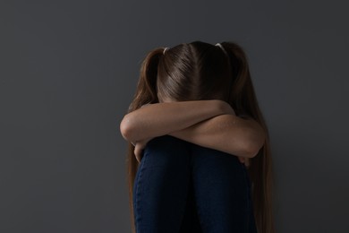 Sad girl sitting near dark grey background, space for text