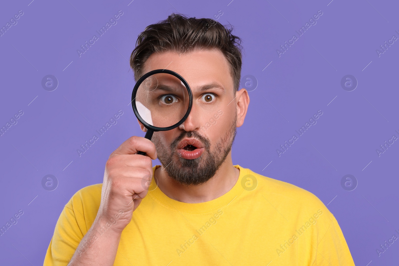 Photo of Emotional man looking through magnifier on violet background