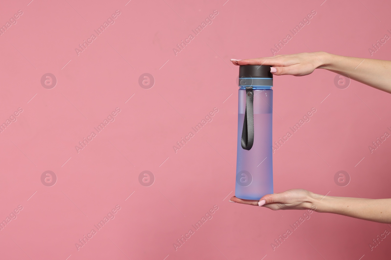 Photo of Woman holding transparent bottle on pink background, closeup. Space for text