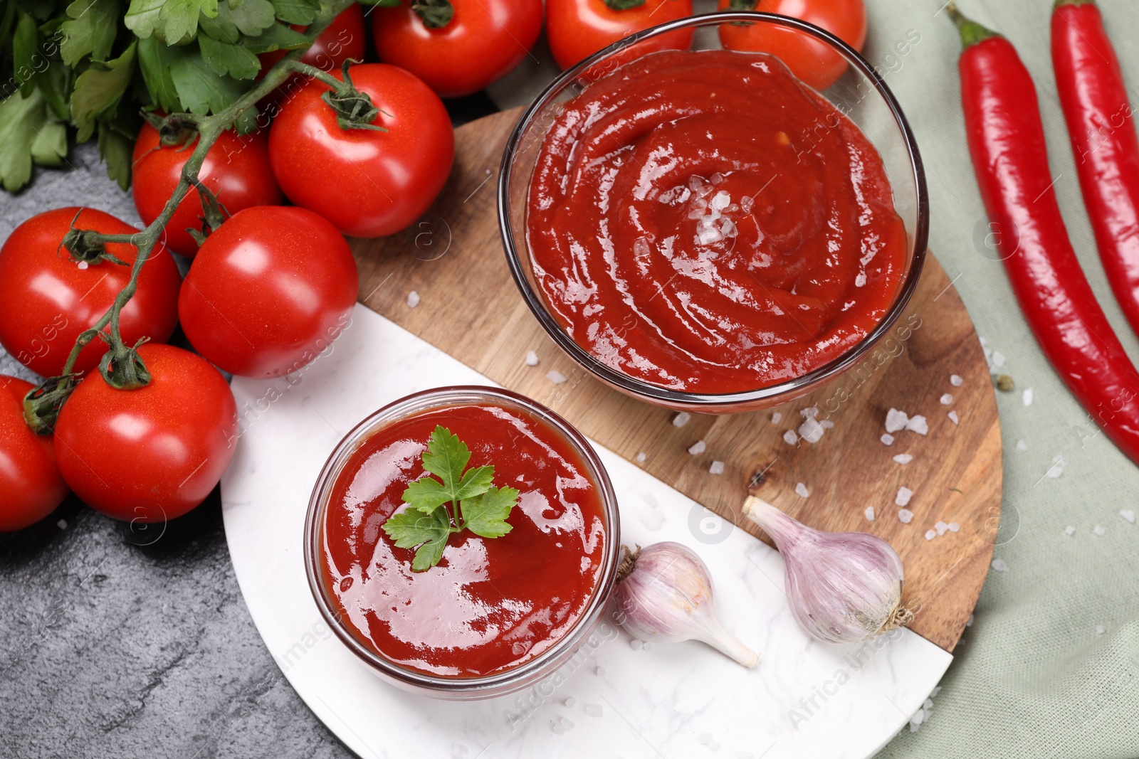 Photo of Organic ketchup in bowls and ingredients on black table, flat lay. Tomato sauce