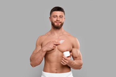 Photo of Handsome man applying body cream onto his chest on light grey background