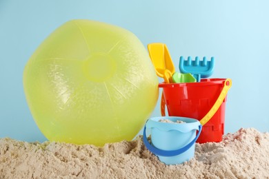 Photo of Bright inflatable ball and plastic beach toys on sand against light blue background