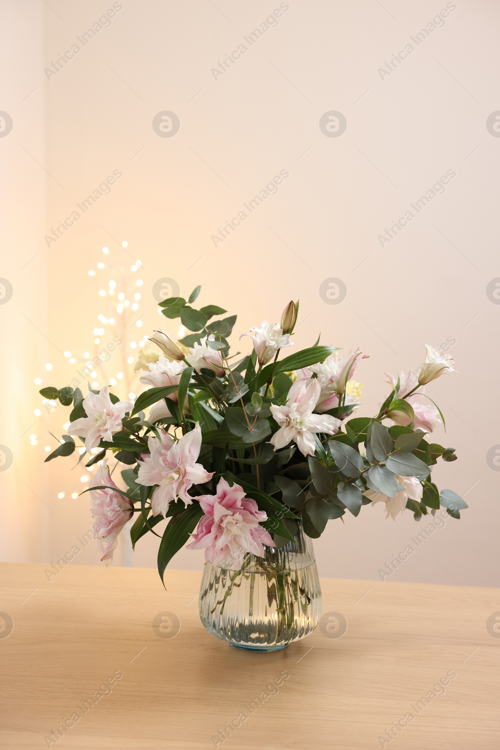 Photo of Bouquet of beautiful lily flowers in vase on wooden table against beige background