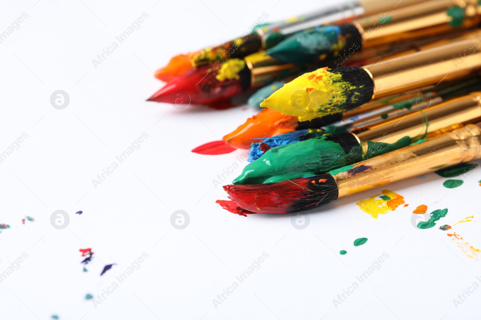 Photo of Brushes with colorful paints on white background, closeup. Space for text