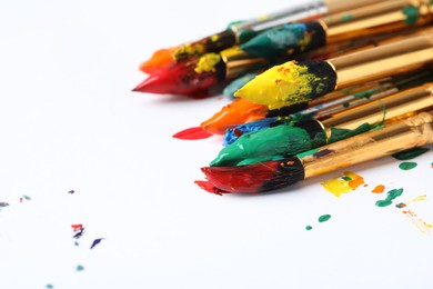 Photo of Brushes with colorful paints on white background, closeup. Space for text