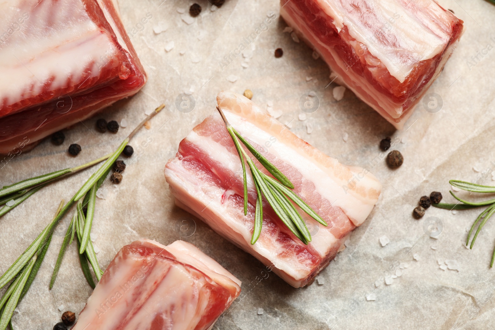 Photo of Raw ribs with rosemary and spices on parchment paper, flat lay