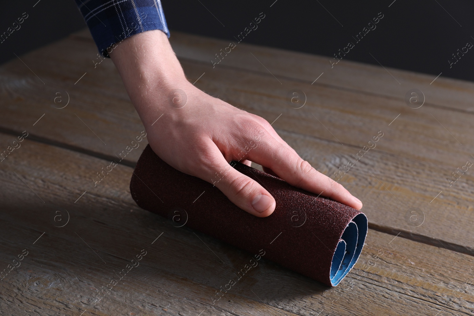 Photo of Man polishing wooden table with rolled sheet of sandpaper, closeup