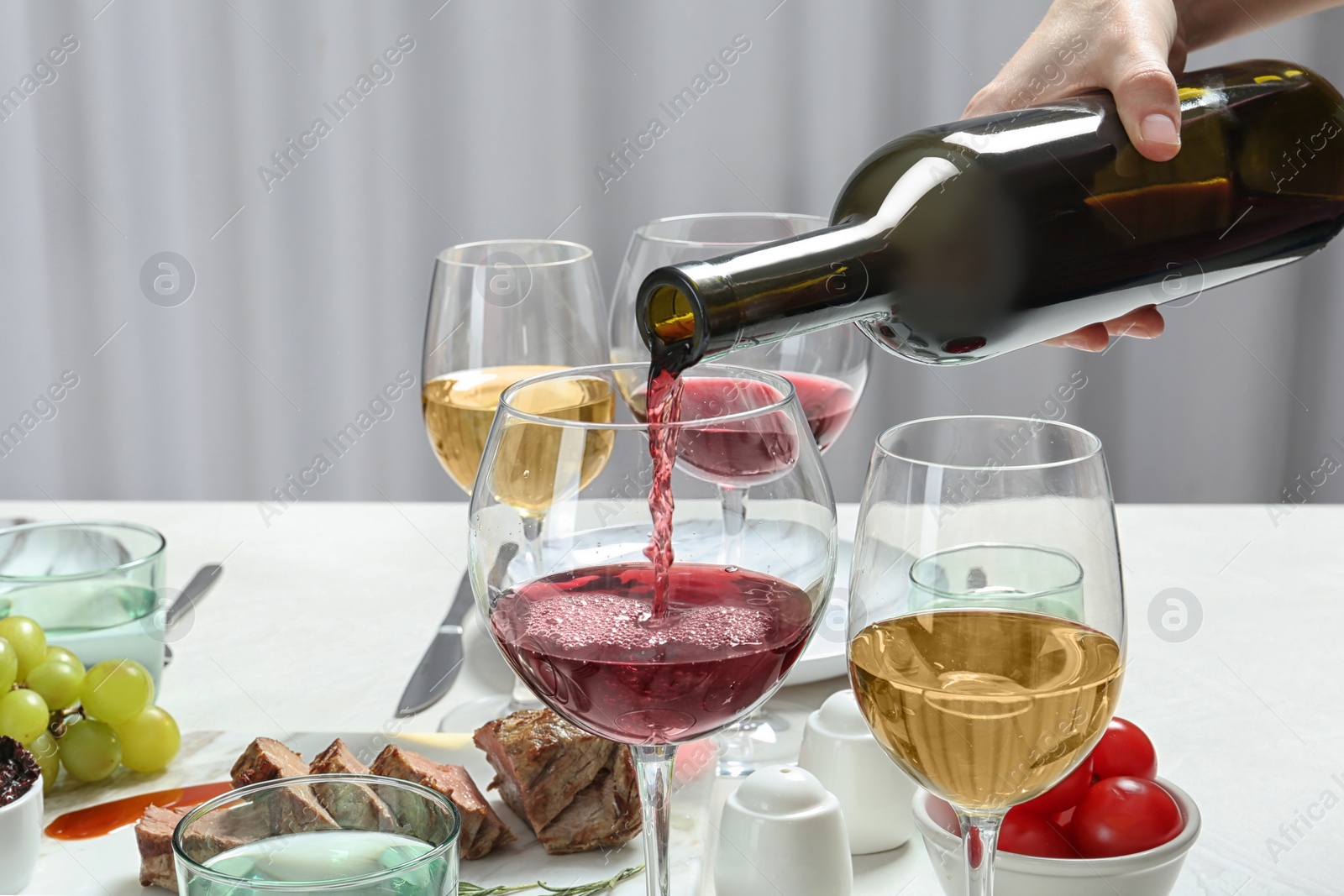 Photo of Woman pouring red wine into glass on served table