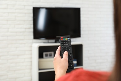 Woman changing TV channel with remote control in living room, focus on hand. Space for text