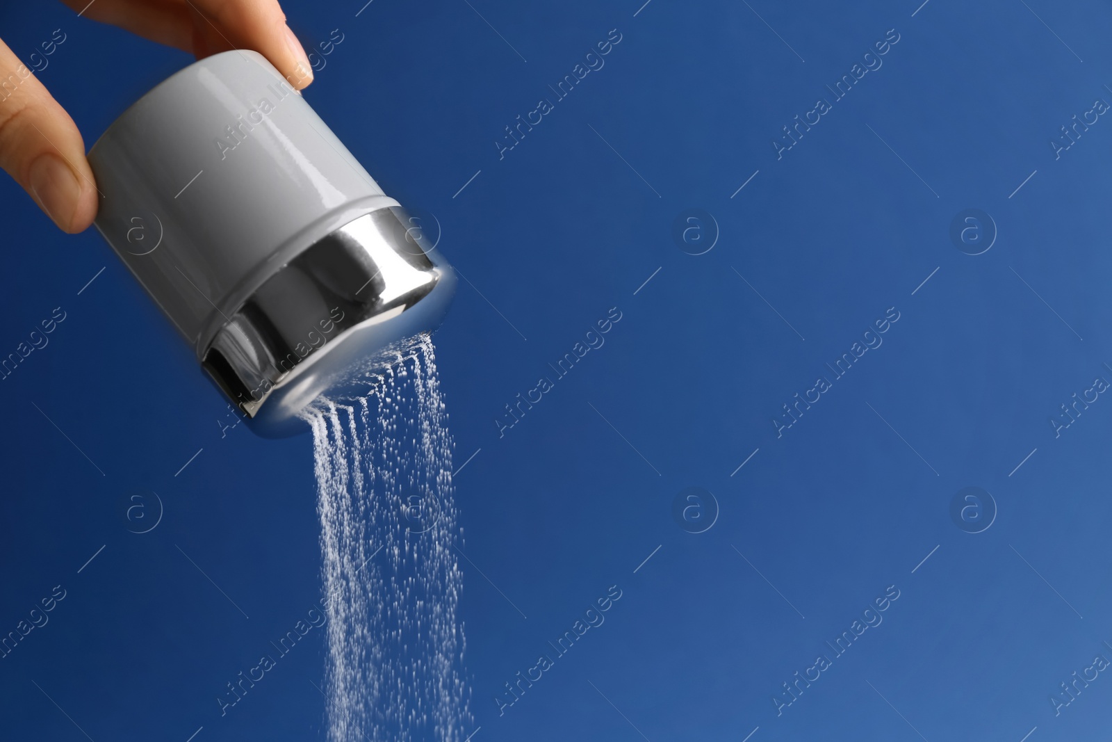 Photo of Woman pouring salt from shaker on blue background, closeup. Space for text