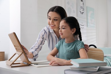 Mother helping her daughter doing homework with tablet at home