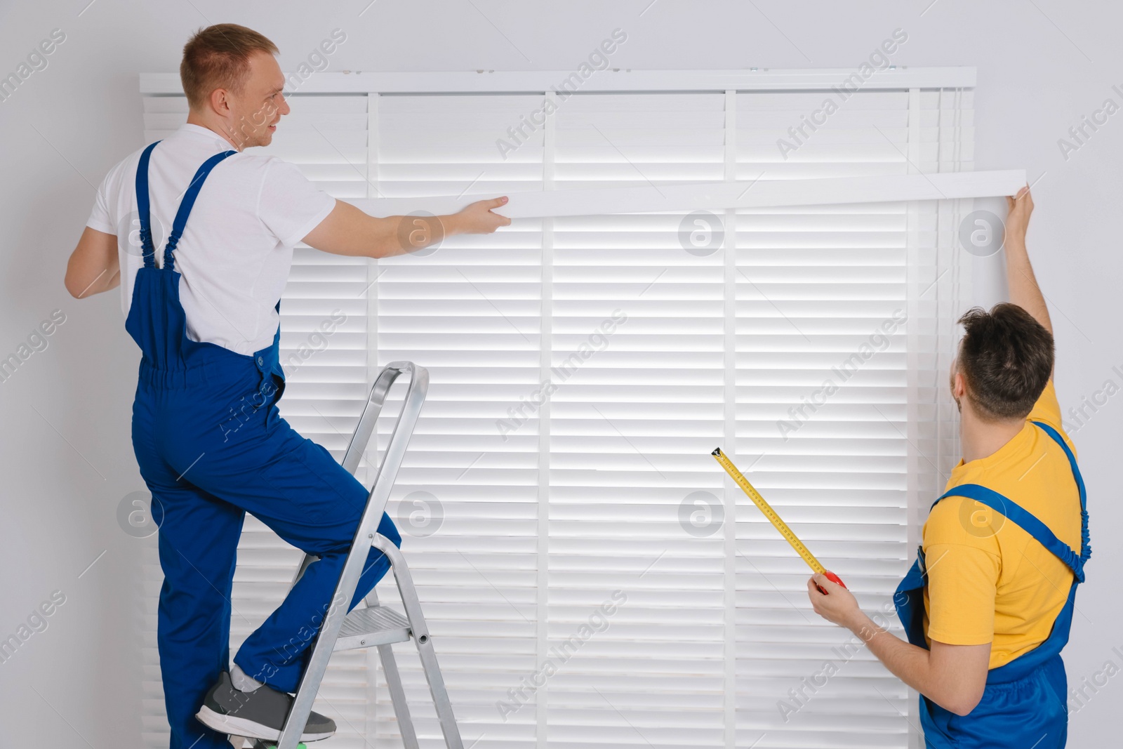 Photo of Workers in uniforms installing horizontal window blinds indoors