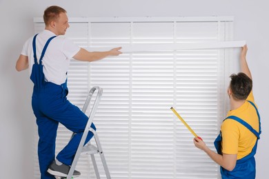 Photo of Workers in uniforms installing horizontal window blinds indoors