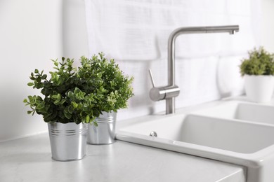 Photo of Artificial potted herbs on white marble countertop near sink in kitchen. Home decor
