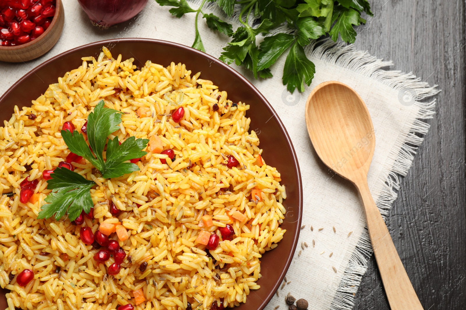 Photo of Tasty rice pilaf with pomegranate grains served on black wooden table, flat lay