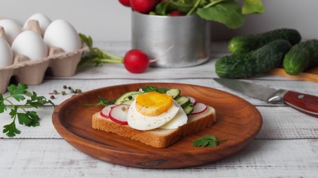 Photo of Tasty sandwich with boiled egg, radish, cucumber and ingredients on white wooden table