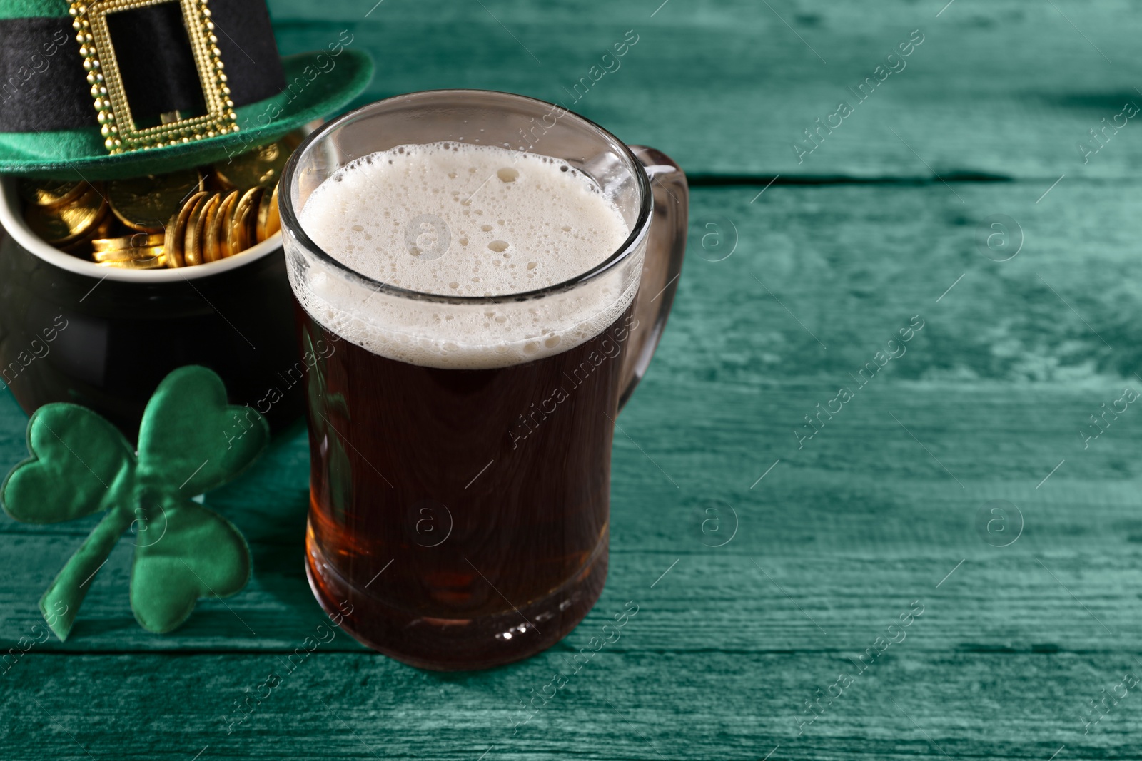 Image of St. Patrick's day. Beer, leprechaun hat, pot of gold and decorative clover leaf on green wooden table. Space for text