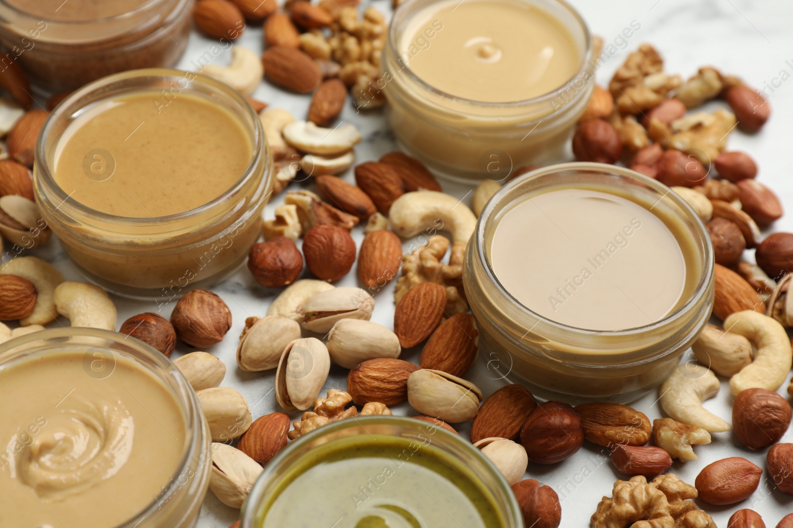 Photo of Jars with butters made of different nuts and ingredients on white marble table, closeup