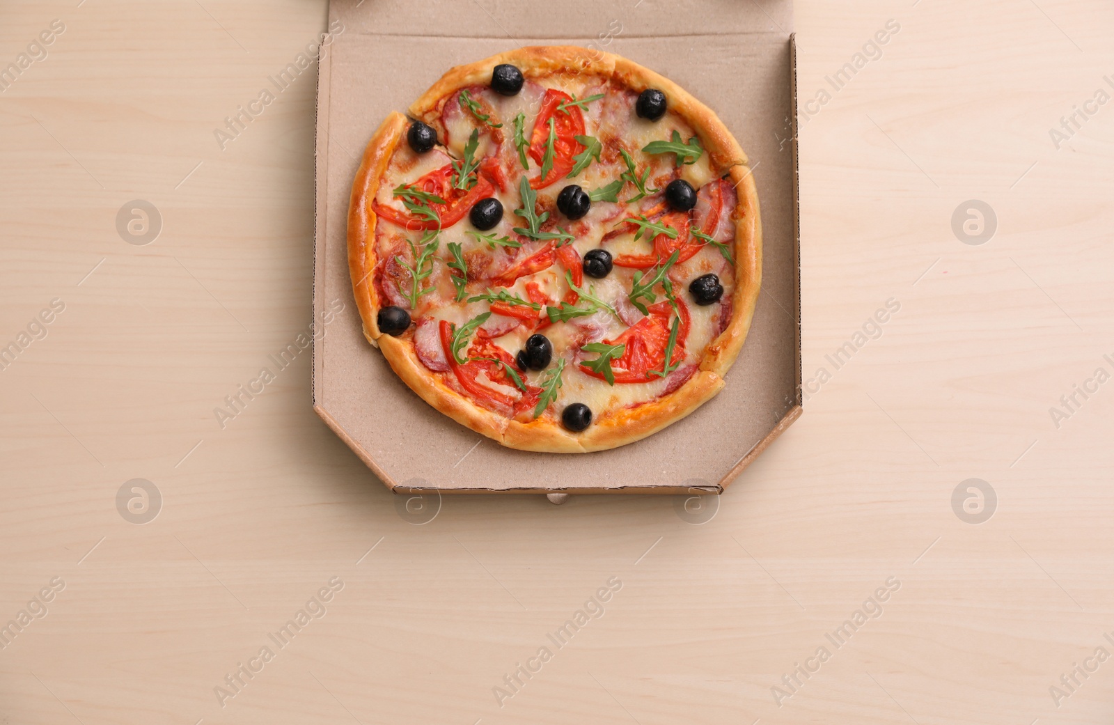 Photo of Cardboard box with tasty pizza on wooden background, top view with space for text