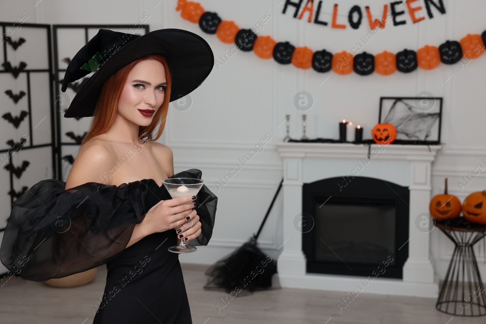 Photo of Young woman in scary witch costume with glass of cocktail indoors, space for text. Halloween celebration