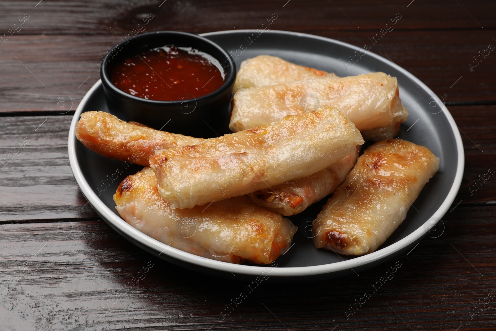 Photo of Tasty fried spring rolls and sauce on wooden table, closeup