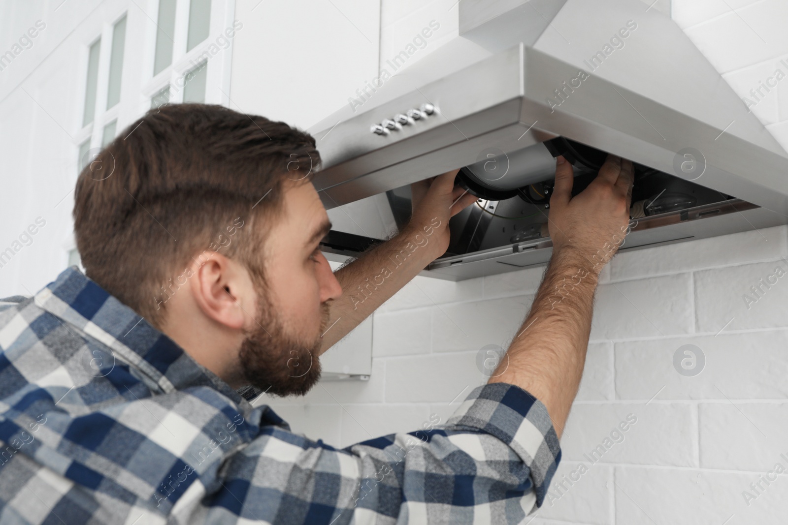 Photo of Man repairing modern cooker hood in kitchen